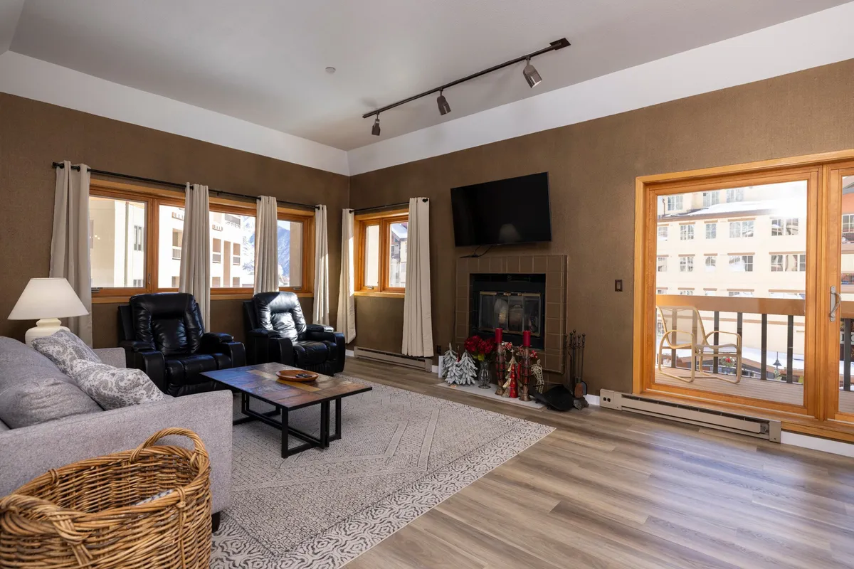 A cozy living area featuring a plush sofa and coffee table arranged in front of a wood-burning fireplace. Large windows reveal panoramic views of the Needles Mountain Range, filling the room with natural light and connecting the interior to the majestic outdoors. The setting is perfect for relaxing, reading, or gathering with friends and family after a day on the slopes.