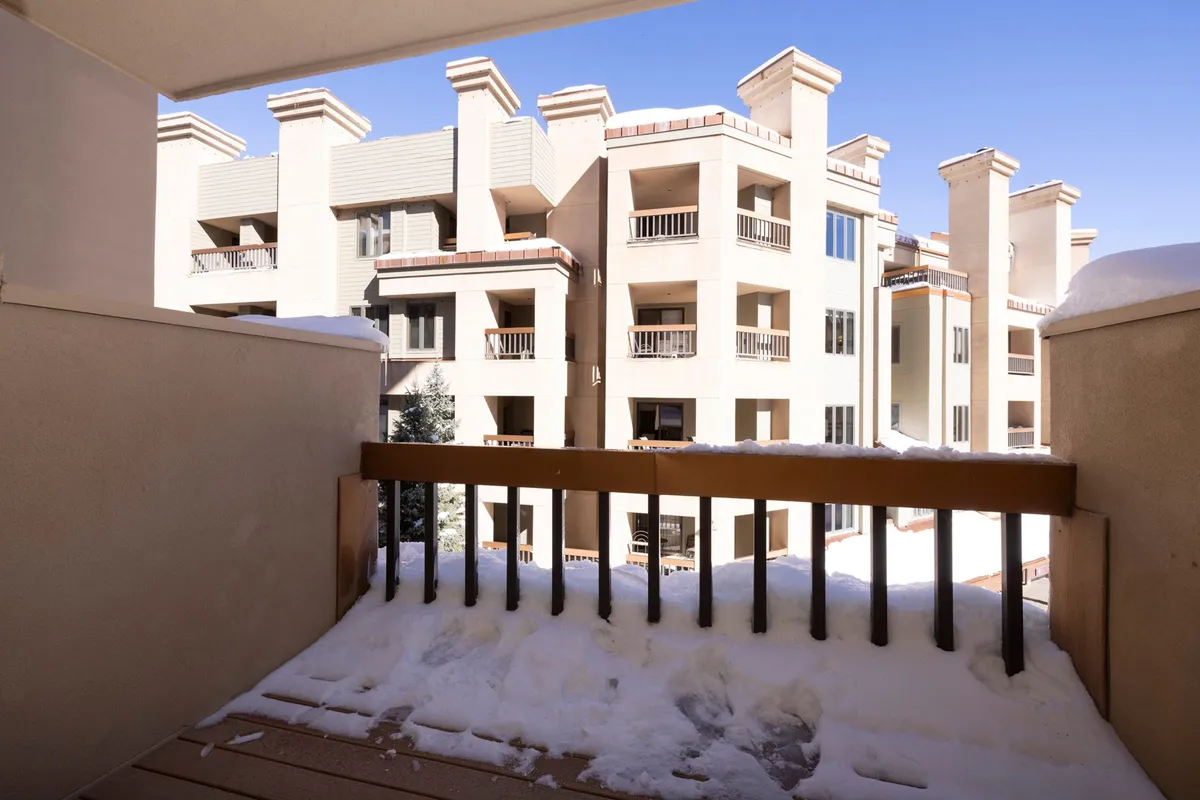 An inviting balcony dusted with snow, with a clear blue sky and adjacent buildings visible, creating a cozy vantage point for relaxing mornings or peaceful evenings. The tranquil environment highlights opportunities to enjoy the outdoors even while at the property.