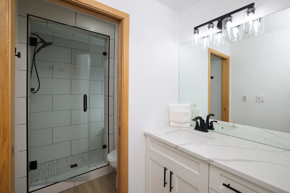 A modern bathroom with a glass shower enclosure, a sleek vanity with a sink, and contemporary light fixtures. The overall mood is refreshing and serene, offering a spa-like experience for guests.